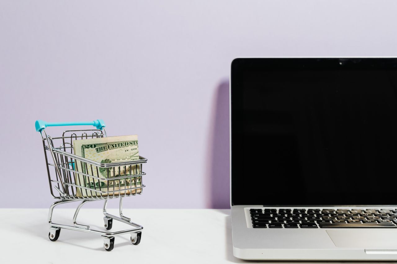 journey-01 Shopping cart with money next to a laptop symbolizing online shopping and e-commerce.