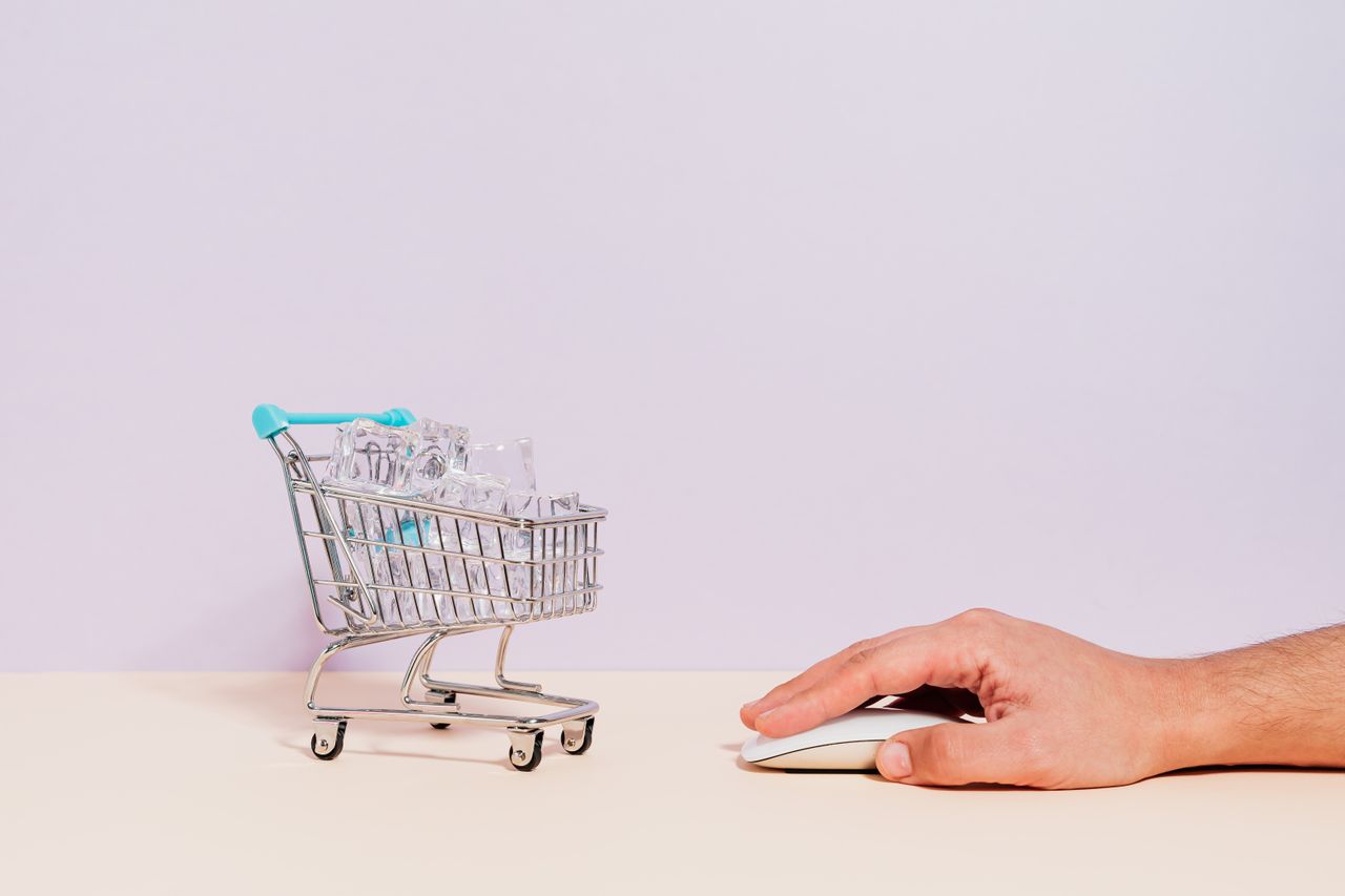 home-img Conceptual image of a hand on a mouse next to a miniature shopping cart filled with ice cubes, symbolizing online shopping.